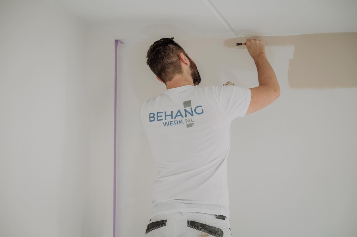 Schilder van Behangwerk schildert een muur in beige